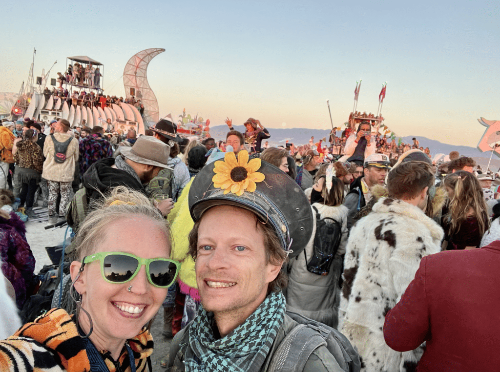 A couple in front of art cars at sunrise at burning Man